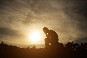 person holding their head in their hands outside with the sun behind them