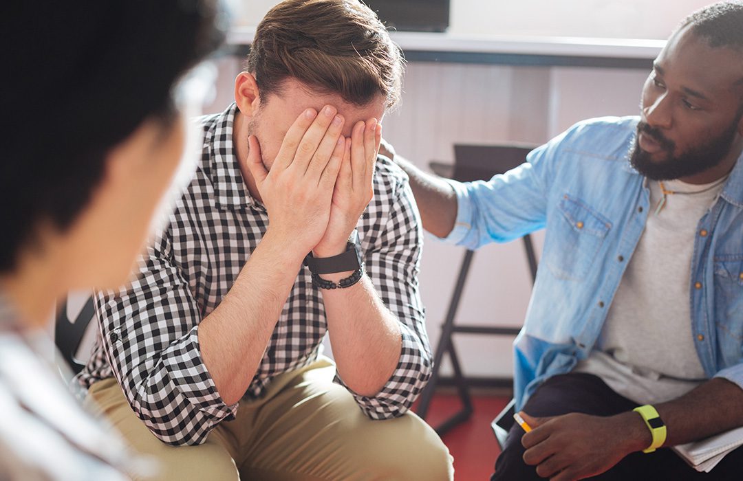 person with hands over their face, other people next to them putting their hands on their back