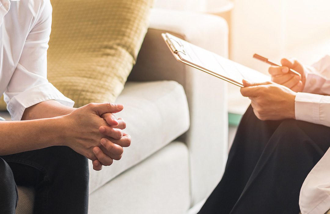 close up of person talking to a doctor or therapist holding a clipboard