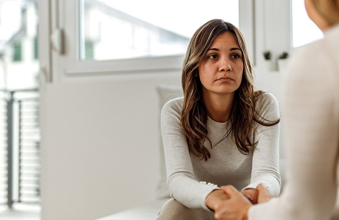 young person sitting on a couch talking to someone and holding their hands