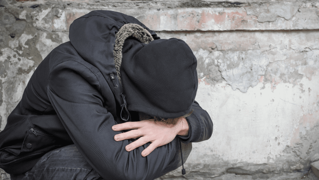 Man with his head in between his knees in an ally