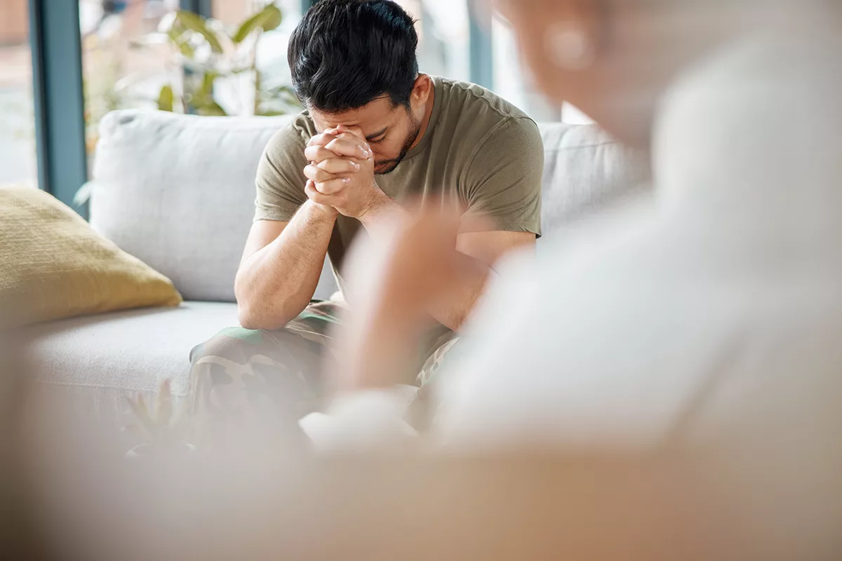 man with hands clasped up to his face talking to therapist or doctor