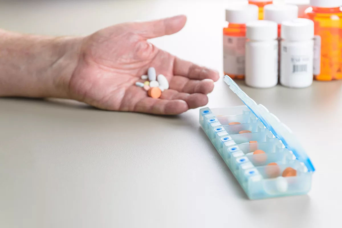 person holding pills next to pill organizer