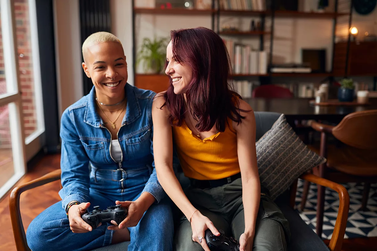 same sex couple sitting on couch together playing video games