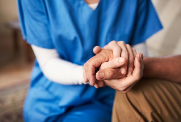A person in blue scrubs gently holds the hand of another person, offering comfort and support.
