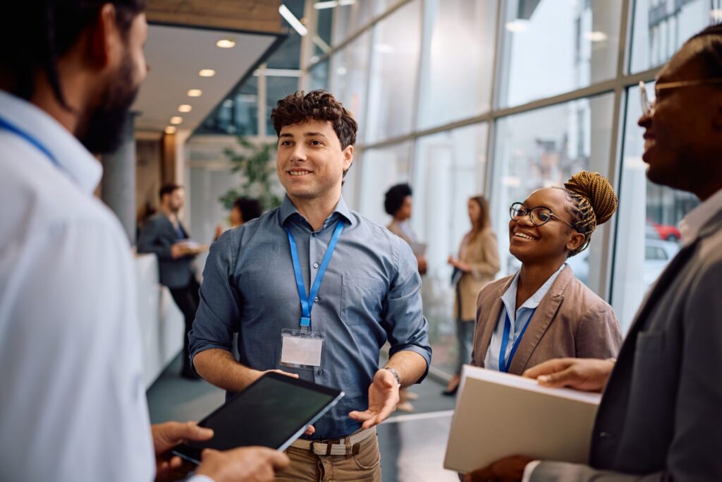 A group of professionals from SummitStone Health Partners wearing name badges and business attire are smiling and conversing in a modern office hallway with large windows. One person is holding a tablet, while another holds folders.